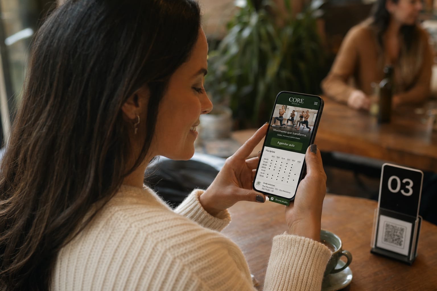 Aluna olhando a Página do Estabelecimento de uma academia no celular em uma cafeteria